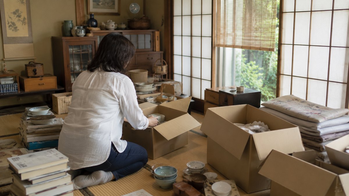 和室で家財を段ボール箱に仕分けして片付けている女性の後ろ姿