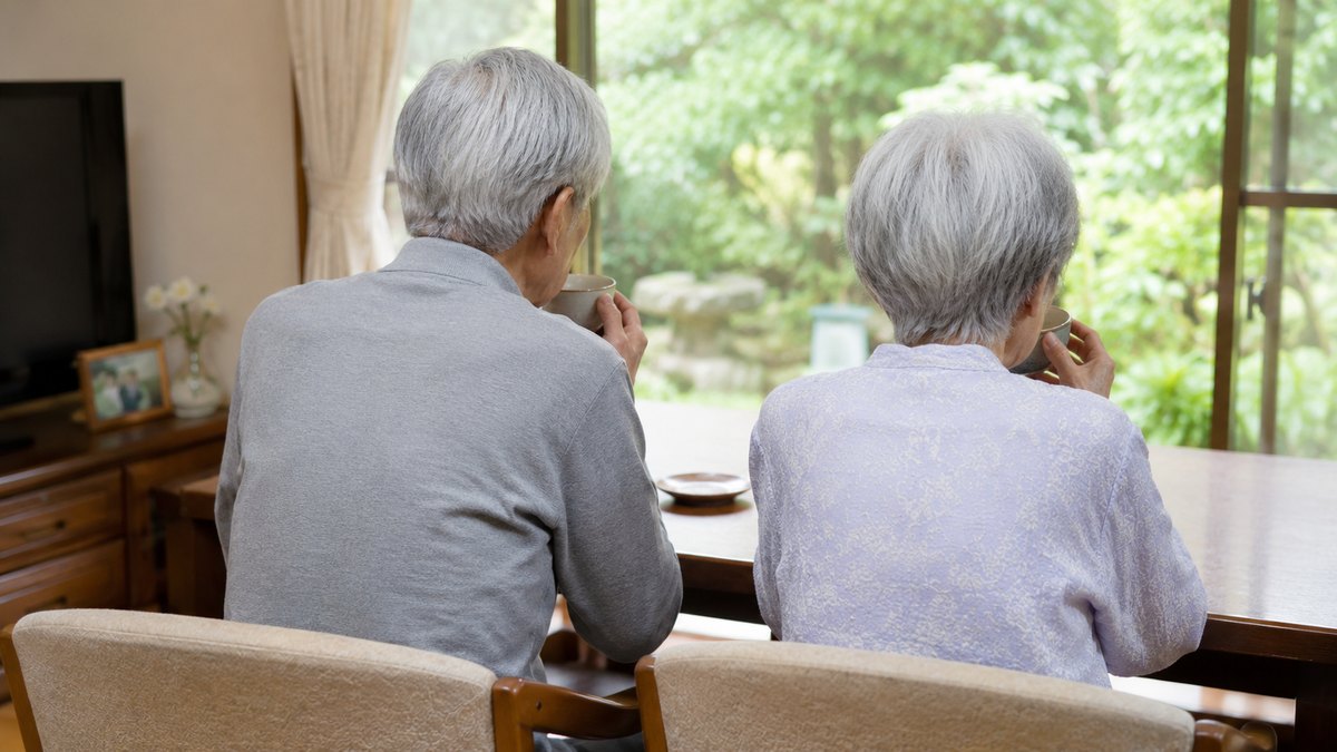 窓辺で並んでお茶を飲む80代の夫婦の後ろ姿