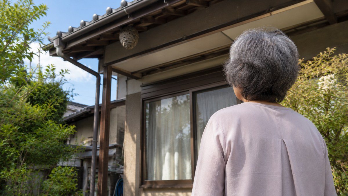 実家の軒下にできた蜂の巣と、庭からそれを見つめる高齢の母の後ろ姿