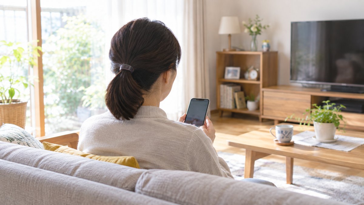 ソファで娘世代の女性がスマートフォンでMANOMAの口コミ・評判を読んでいる後ろ姿