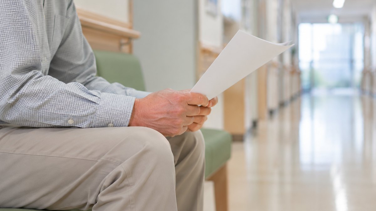 病院の廊下のベンチで介護保険申請の書類を持つ50代男性の手元