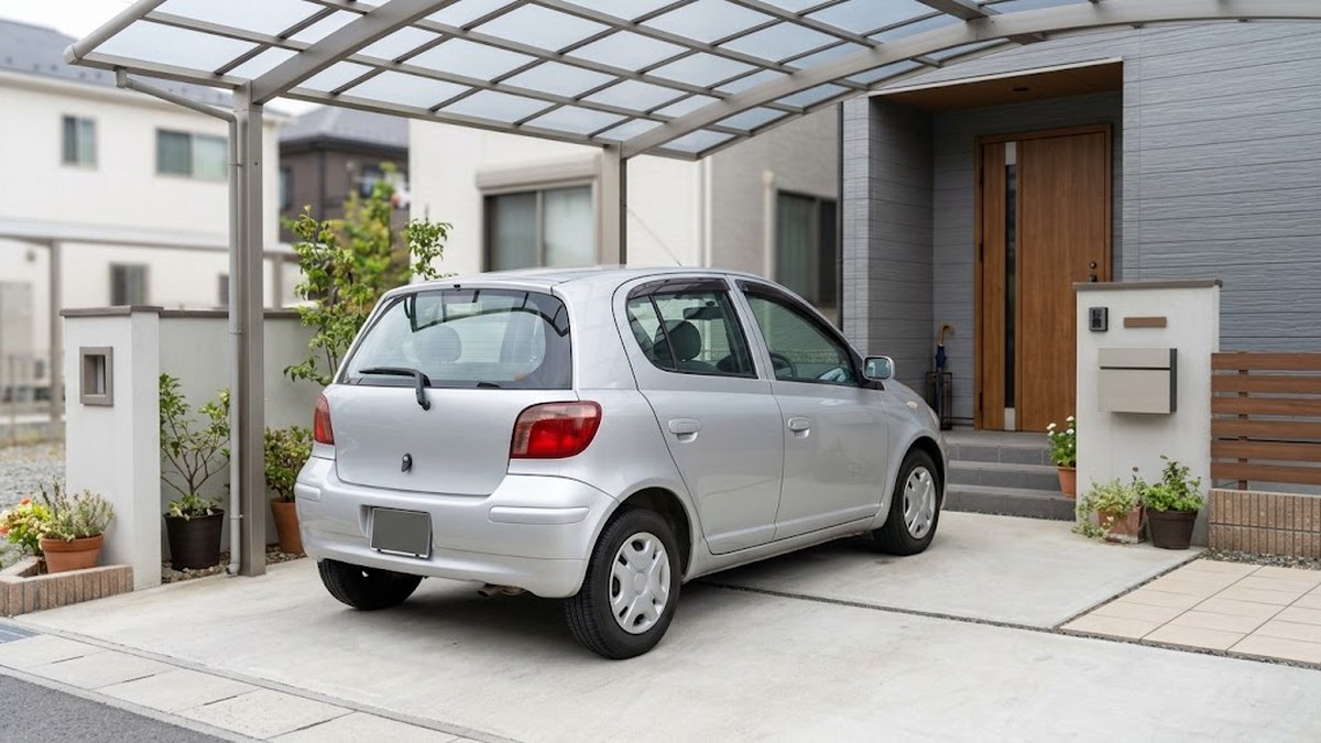 戸建ての駐車場に止めた、年式は古いがきれいな普通乗用車（車種が分からない角度）